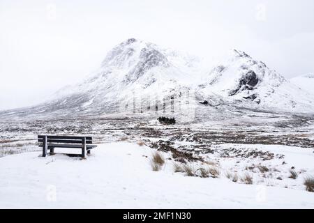 Holzbank mit Winterblick auf das schneebedeckte Buachaille Etive Mor. Glencoe, Scottish Highlands, Großbritannien. Stockfoto