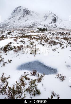 Wunderschöne schneebedeckte Landschaft mit gefrorener Pfütze und Blick auf den berühmten Berg in Glencoe, Scottish Highlands, Großbritannien. Stockfoto