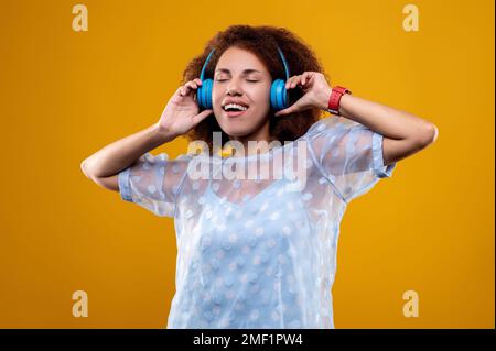 Süße junge Frau in Weiß, die der Musik zuhört und aufgeregt aussieht Stockfoto