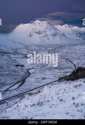 Lange kurvenreiche Straße durch das schneebedeckte Tal von Glencoe, Großbritannien. Stockfoto