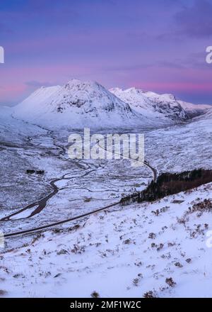 Schneebedeckte Berge von Glencoe bei Sonnenaufgang mit kurviger Straße, die durch die Landschaft führt. Scottish Highlands, Großbritannien. Stockfoto