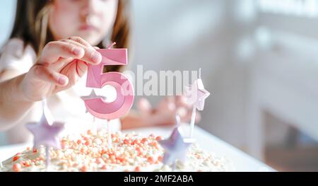 Große rosa Kerze mit 5 Ziffern auf hausgemachtem Kuchen. Kreative Gratulation zu fünf Jahren für ein Mädchen. Festliche Dekoration zum 5. Geburtstag, Belag, Dressi Stockfoto