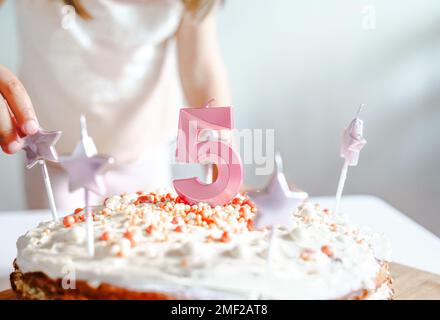 Große rosa Kerze mit 5 Ziffern auf hausgemachtem Kuchen. Kreative Gratulation zu fünf Jahren für ein Mädchen. Festliche Dekoration zum 5. Geburtstag, Belag, Dressi Stockfoto