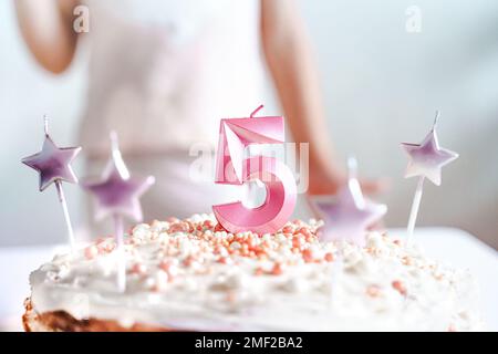 Große rosa Kerze mit 5 Ziffern auf hausgemachtem Kuchen. Kreative Gratulation zu fünf Jahren für ein Mädchen. Festliche Dekoration zum 5. Geburtstag, Belag, Dressi Stockfoto