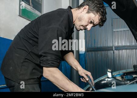 Mechaniker mit Spannungsprüfer-Schraubendreher während der Prüfung der Fahrzeugbatterie in der Werkstatt Stockfoto