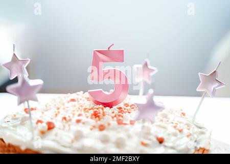 Große rosa Kerze mit 5 Ziffern auf hausgemachtem Kuchen. Kreative Gratulation zu fünf Jahren für ein Mädchen. Festliche Dekoration zum 5. Geburtstag, Belag, Dressi Stockfoto