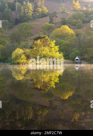 Das rustikale Bootshaus spiegelt sich an einem frischen Frühlingsmorgen in einem ruhigen, friedlichen See wider. Rydal Water, Lake District, Großbritannien. Stockfoto