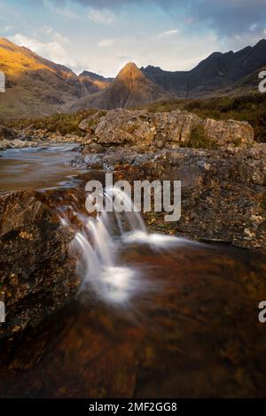 Kleiner tropfender Wasserfall mit atemberaubendem Blick auf die Cuillin-Berge in goldenem Licht. Fairy Pools, Isle of Skye, Schottland, Großbritannien. Stockfoto