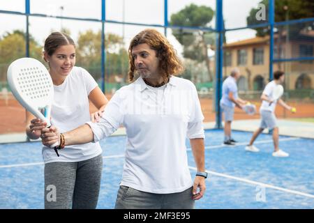 Mädchen, die einem Mann Padel-Tennis auf dem Platz beibringen Stockfoto