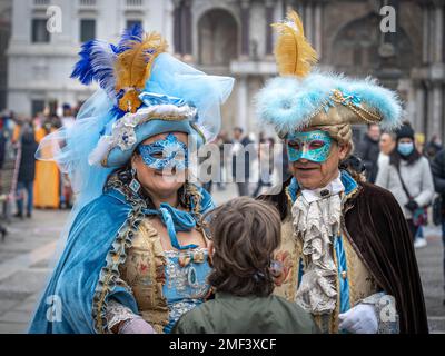Senioren und Senioren in mittelalterlichen Karnevalskostümen und -Masken sprechen mit einem Jungen auf der Piazza San Marco in Venedig Stockfoto