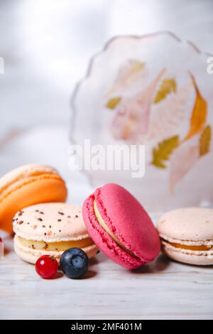 Macaron-Pink, Orange und Beige, Blau auf Marmor. Ein wunderschönes französisches Dessert. Früchte und Epoxidharz und Blumen im Hintergrund. Stockfoto