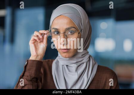 Nahaufnahme. Porträt einer jungen, schönen Araberin im Hijab. Er sieht selbstbewusst in die Kamera und stützt seine Brille mit der Hand. Stockfoto