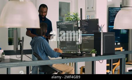 Verschiedene Programmierer arbeiten gemeinsam an der Codierung von Projekten zur Kompilierung von Algorithmen für die neue Cloud-Computing-Benutzeroberfläche auf Computermonitoren. Ein Team von Software-Ingenieuren, das Ideen sammelt. Stockfoto