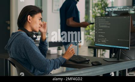 Asiatischer Datenbankprograf, der Code auf einem Computer schreibt und einen Algorithmus für künstliche Intelligenz anzeigt. Softwareentwickler, der an der Codierungsschnittstelle mit Serverinformationen und Big Data arbeitet. Stockfoto