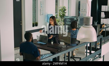 Verschiedene Programmierer sprechen über Quellcode im Terminalfenster und verwenden HTML-Skript, um eine neue Schnittstelle zu erstellen. Team von IT-Ingenieuren, die Algorithmen ausführen, die Datenbank überprüfen und Teamarbeit leisten. Stockfoto