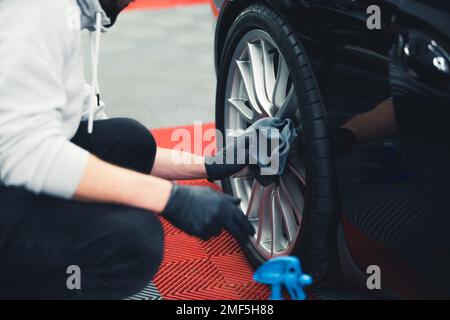 Ein unbekannter Mann mit schwarzen Handschuhen, der Autorad mit einem Lappen putzte, nachdem er die Reifen geschwärzt hatte. Professionelle Fahrzeugdetails. Horizontale Indoor-Aufnahme. Hochwertiges Foto Stockfoto