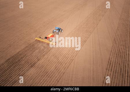 Ein Traktor mit einer Sämaschine auf dem Feld, Dröhnensaison der Aussaat. Stockfoto