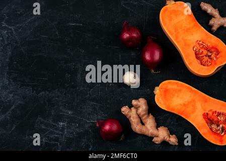 Roher Butternusskürbis mit roten Zwiebeln, Ingwer und Knoblauch auf schwarzem Hintergrund. Zutaten für Kürbissuppe. Draufsicht, flach liegend, Kopierbereich. Stockfoto