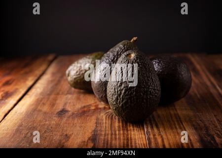 Mexikanische Avocado (Persea americana) auf rustikalem Holztisch. Hauptbestandteil zur Zubereitung von Guacamole. Nahaufnahme des Bildes mit Kopierbereich. Stockfoto