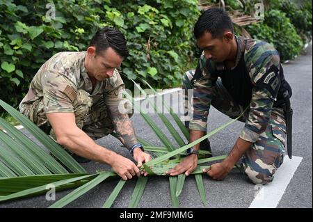 Ein Lehrer beim Royal Malaysian Air Force Jungle Warfare Training Center unterrichtet die USA Air Force Tech Sgt. Casey Carter, 18. Operations Support Squadron Survival, evasion, Resistance and Escape (SERE) Specialist, ihre Technik zum Weben von Bambusfronten als Unterschlupf während eines Expertenaustauschs zum Überleben des Dschungels im Rahmen der Übung Pacific Angel 22 in Jugra Hill, Malaysia, 18. August 2022. SERE-Spezialisten werden mehr als ein Jahr lang geschult, um Experten in den Fähigkeiten zu werden, die notwendig sind, um in jedem Biom zu überleben, einschließlich Dschungel, Tundra, gemäßigten und städtischen Umgebungen. Stockfoto