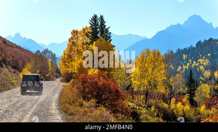 Herbstfahrt - Ein SUV, der an einem sonnigen Herbstmorgen auf einer landschaftlich reizvollen Straße durch das Hinterland in Richtung der zerklüfteten Sneffels Range fährt. Uncompahgre National Forest. Stockfoto