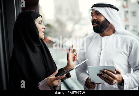 Genau der Mann, mit dem ich sprechen wollte. Zwei junge Geschäftsleute, die traditionelle islamische Kleidung tragen und ihre Tablets auf dem Balkon des Büros benutzen. Stockfoto