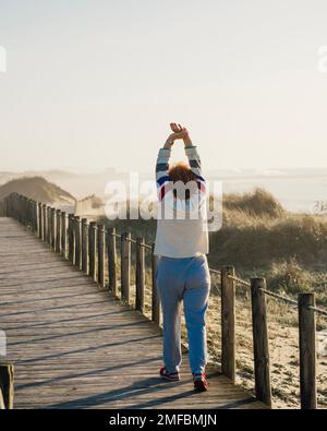 Reife Frau Übung am Morgen, Erwachsene Frau dehnt Muskeln gegen die Dünen am Strand, Aufwärmen. Aktives Lifestyle-Konzept. Stockfoto