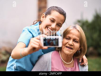 Ich tue mein Bestes, um ihr Leben angenehmer zu machen. Ein Betreuer macht draußen ein Selfie mit einem Seniorpatienten. Stockfoto