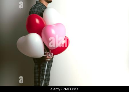 Aufblasbare Heliumballons in Form eines Herzens zum Valentinstag werden von einem Mann gehalten. Vorderansicht. Stockfoto