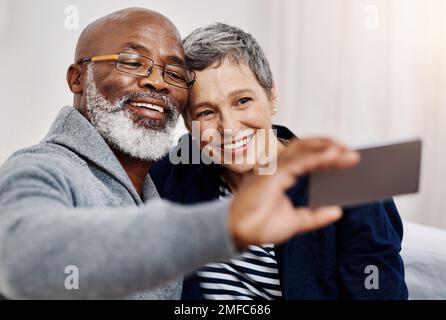 Posiere für die Kamera-Liebste. Ein liebevolles Seniorenpaar, das Selfies macht, während es sich zu Hause auf dem Sofa entspannt. Stockfoto