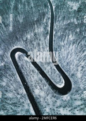 Luftaufnahme einer kurvenreichen Straße durch den schneebedeckten Wald. Fantastische kurvenreiche Straße von oben. Stockfoto