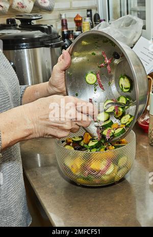 Der Koch gibt den Salat mit Zucchini, Orangen und Salami aus der Schüssel in die Salatschüsseln. Französische Gourmetküche, Holzhintergrund Stockfoto