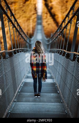 Junge blonde, modische Frau, die auf einer Hängebrücke in Österreich stand, Highline179. Stockfoto