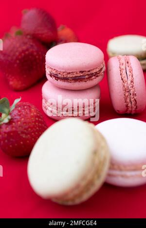 Nahaufnahme Porträtstudio mit leckeren bunten französischen Makronen-Keksen auf rotem Hintergrund mit Erdbeeren. Stockfoto