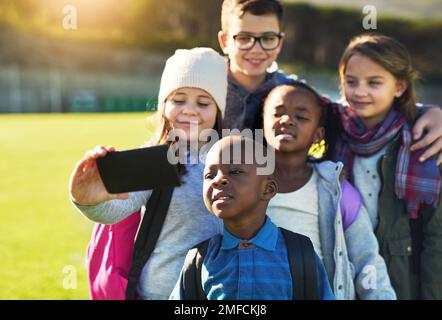 Alle versammeln sich für die Film-Jungs. Eine Gruppe von Grundschulkindern, die zusammen ein Selfie auf dem Rasen der Schule machen. Stockfoto