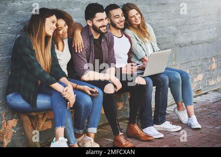 Glückliche Zeiten sind noch glücklicher, wenn sie geteilt werden. Eine Gruppe junger Freunde, die ihre Wireless-Geräte gemeinsam im Freien nutzen. Stockfoto