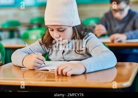 Konzentrierte sich darauf, ihre Schulaufgaben zu erledigen. Ein Mädchen aus der Grundschule, das im Klassenzimmer arbeitet. Stockfoto