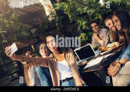 Wir können das im Pausenraum aufhängen. Eine Gruppe kreativer Mitarbeiter, die bei einem Geschäftstreffen im Freien Selfies machen. Stockfoto