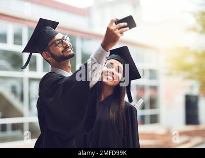 Die Leute sagen, man soll sich nicht beim Lernen verabreden, wir haben es ihnen gezeigt. Zwei Absolventen machen ein Selfie zusammen. Stockfoto