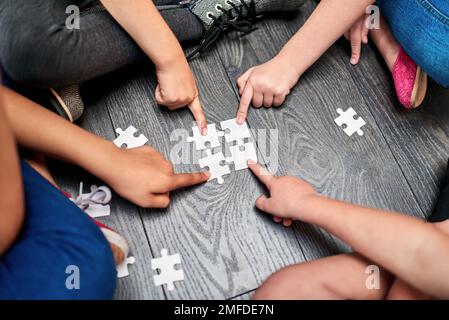 Das perfekte Spiel zur Unterstützung des Lernprozesses. Aufnahmen aus dem Blickwinkel einer Gruppe von nicht wiedererkennbaren Kindern, die zusammen ein Puzzle bauen, während sie auf dem sitzen Stockfoto