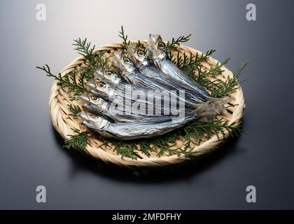 Ulmae-Sardinen in einem Sieb auf schwarzem Hintergrund serviert. Japanisches Essen, getrockneter Fisch. Stockfoto