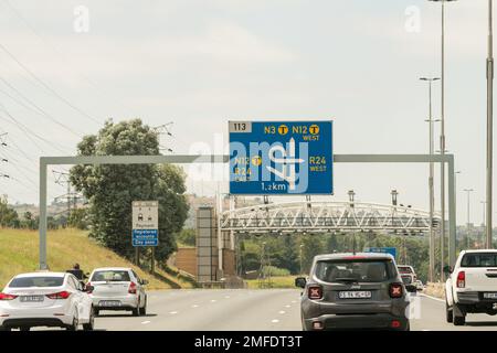 Blaue Autobahnschilder und Autos, Verkehr auf einer Mautstraße, kurz bevor sie unter einer Gantry fahren, um Mautgebühren in Gauteng, Südafrika, zu erheben Stockfoto