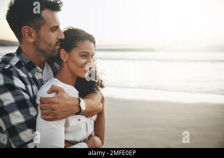 Nichts kommt der Liebe, die wir teilen, nahe. Ein junger Mann umarmt seine Freundin von hinten, während er den Tag draußen verbringt. Stockfoto