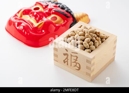 Bohnen zum Bohnenwerfen und Masken von Ogern auf weißem Hintergrund. Japanische Oger. Setsubun-Bild. Stockfoto