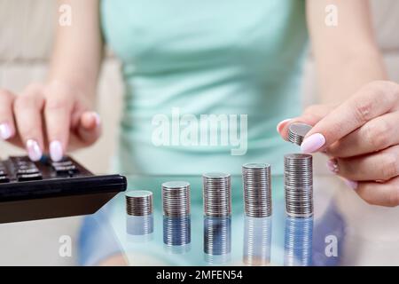 Frau legt Münzen auf einen Stapel von Münzen und zählt auf einem Rechner Stockfoto