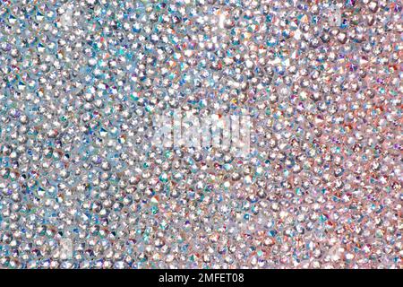 Abstrakter Strasssteinhintergrund. Textur von Strasssteinen, die mit mehrfarbigem Licht beleuchtet werden. Rosa und blaue glänzende Diamanten. Schließen. Leuchtfackeln auf Glas. Stockfoto