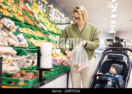 Casualy kleidete die Mutter, die Obst und Gemüse im Supermarkt kaufte, zusammen mit ihrem kleinen Jungen im Kinderwagen Stockfoto