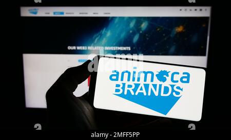 Person, die ein Mobiltelefon mit dem Logo des Softwareunternehmens Animoca Brands Corporation Ltd. Auf dem Bildschirm vor der Webseite hält. Konzentrieren Sie sich auf das Display des Telefons. Stockfoto