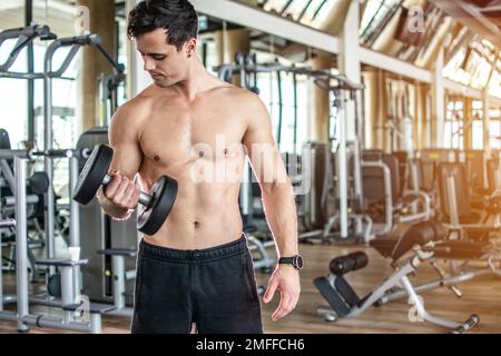 Junger Mann, der die Kurzhantel hebt und im Fitnessstudio an seinem Bizeps trainiert. Stockfoto