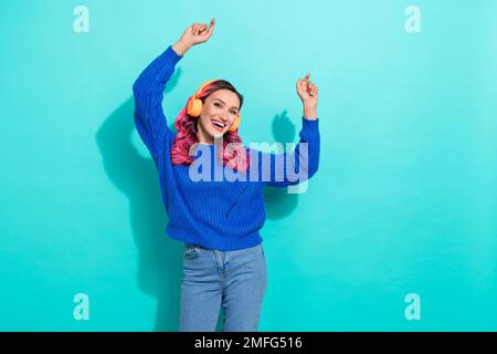 Porträt einer leuchtend positiven, süßen, netten Frau trägt gestrickte Pullover-Kopfhörer und tanzt mit Spaß isoliert auf einem lebendigen blaugrünen Hintergrund Stockfoto